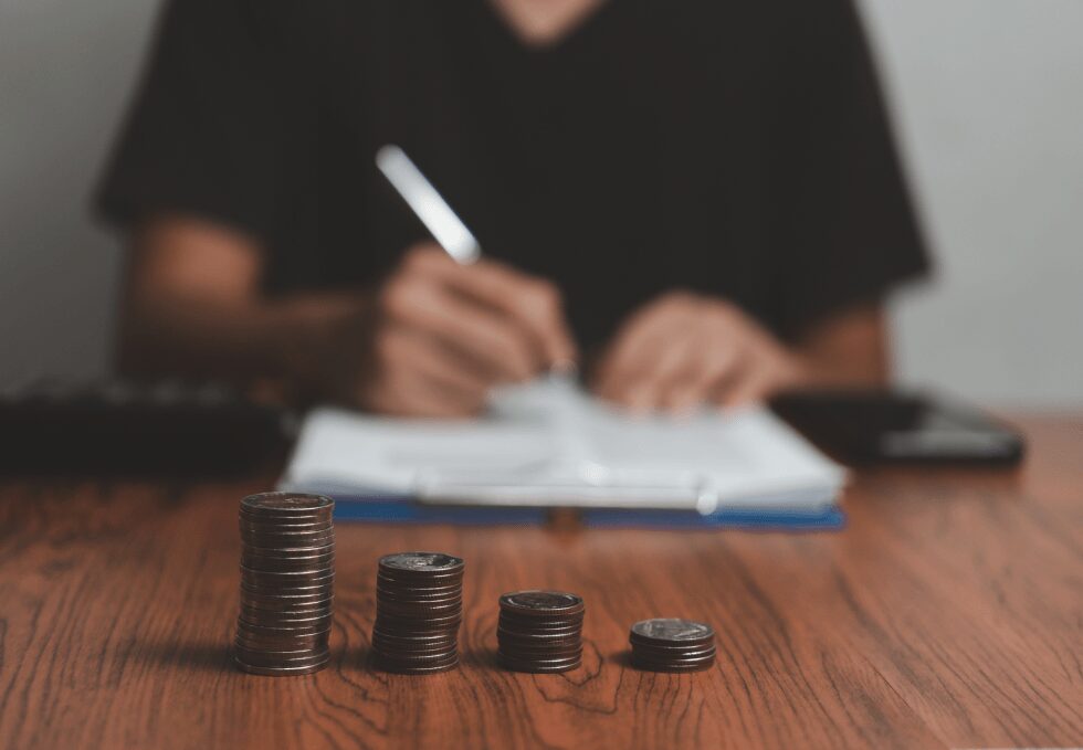 Čtyři sloupce mincí různé výšky před osobou zapisující poznámky do sešitu.